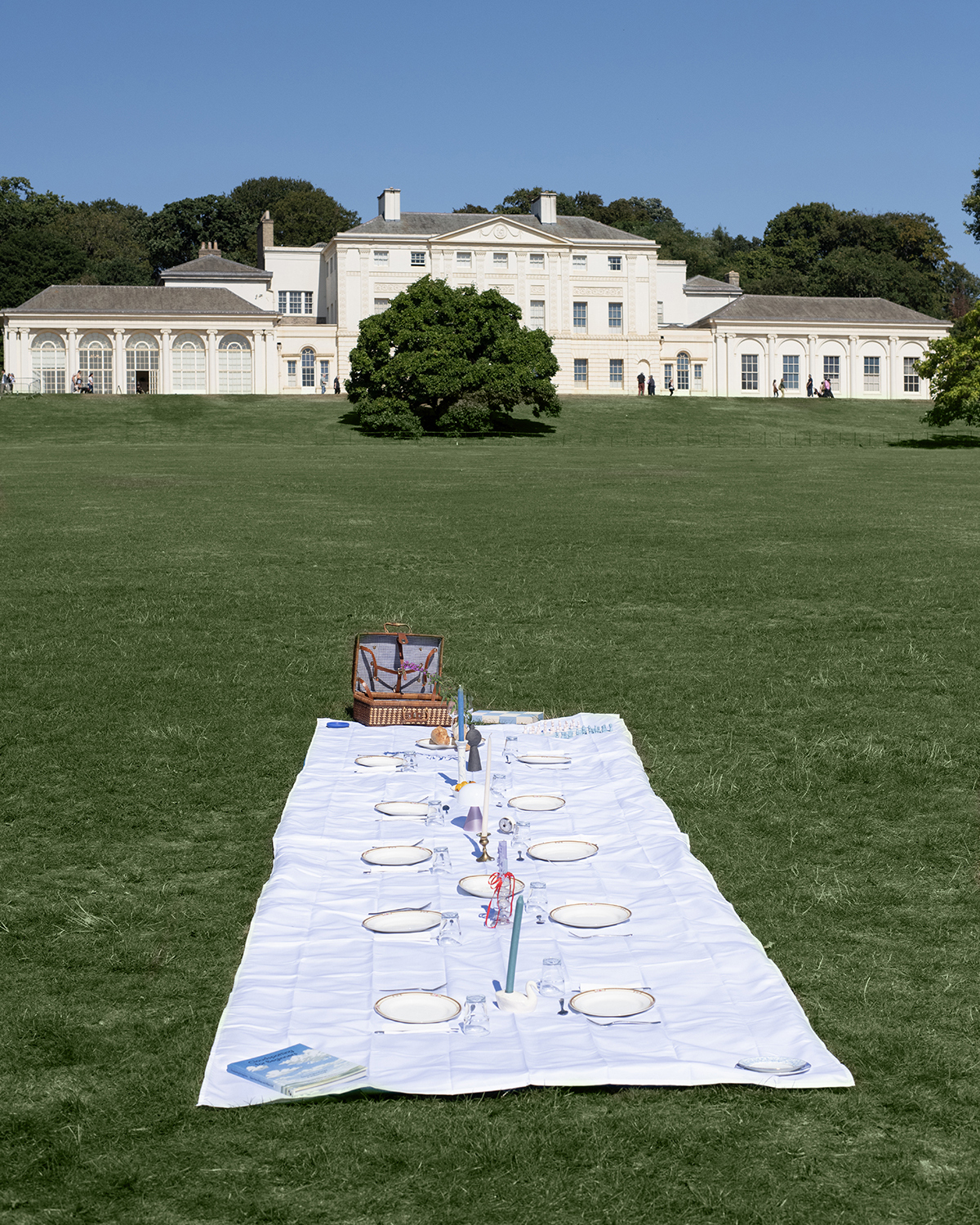 An exquisitely fancy picnic on the lawn in front of a grand mansion during summertime.